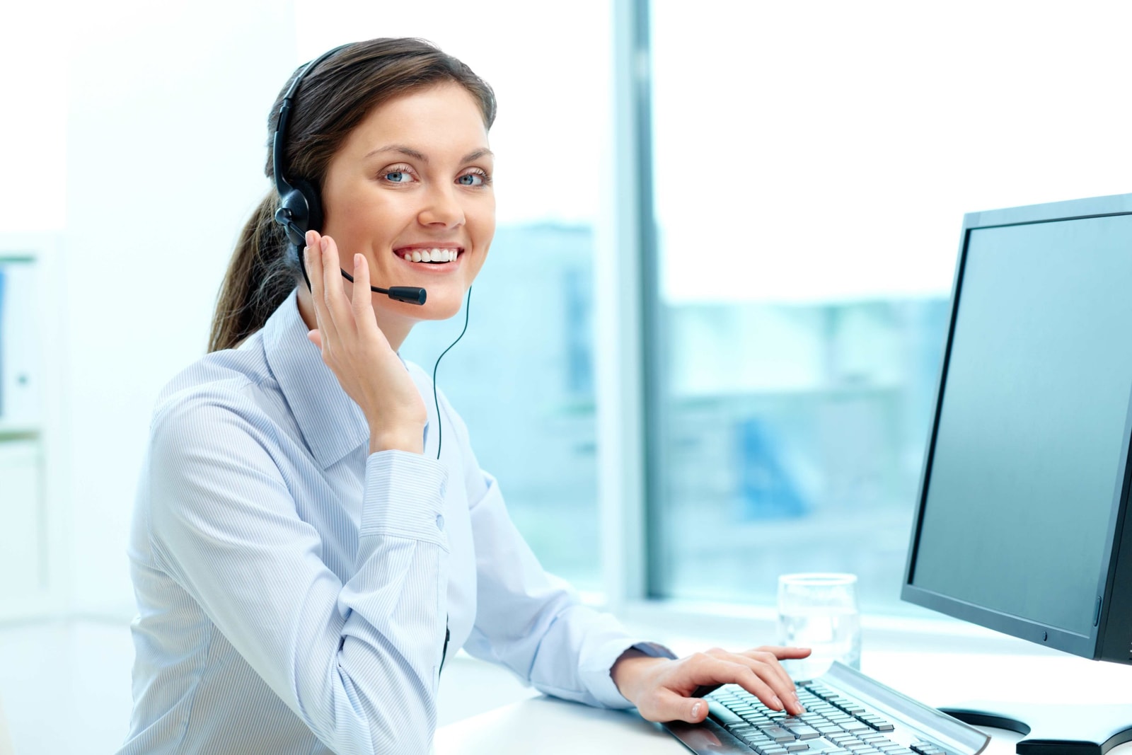 Portrait of young operator with headset looking at camera with friendly smile
