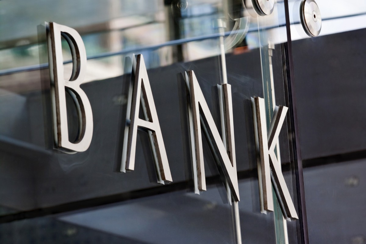 Modern metal Bank sign lettering fixed to a glass wall, with reflections in the glass.
